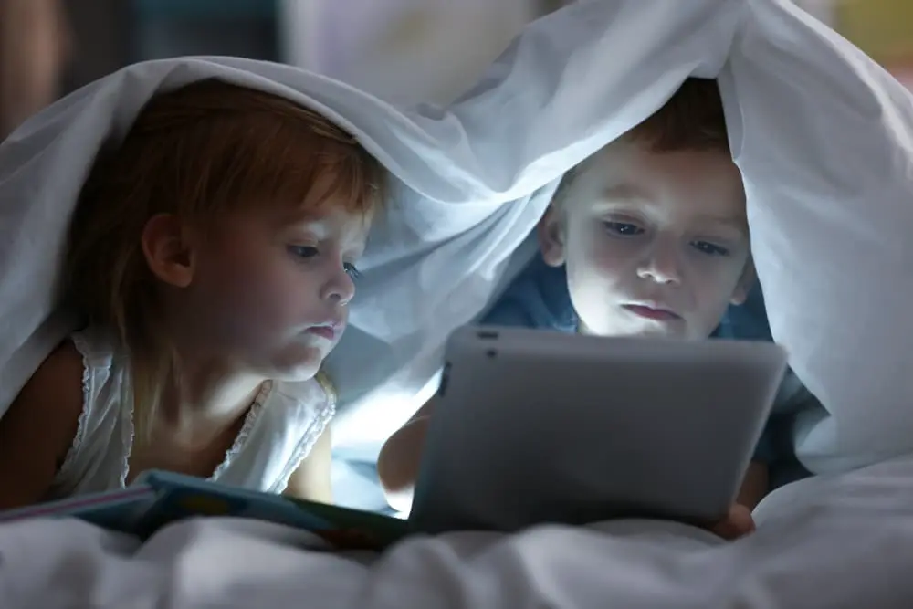 Image of children under duvet looking at a a tablet. Screen time for kids.